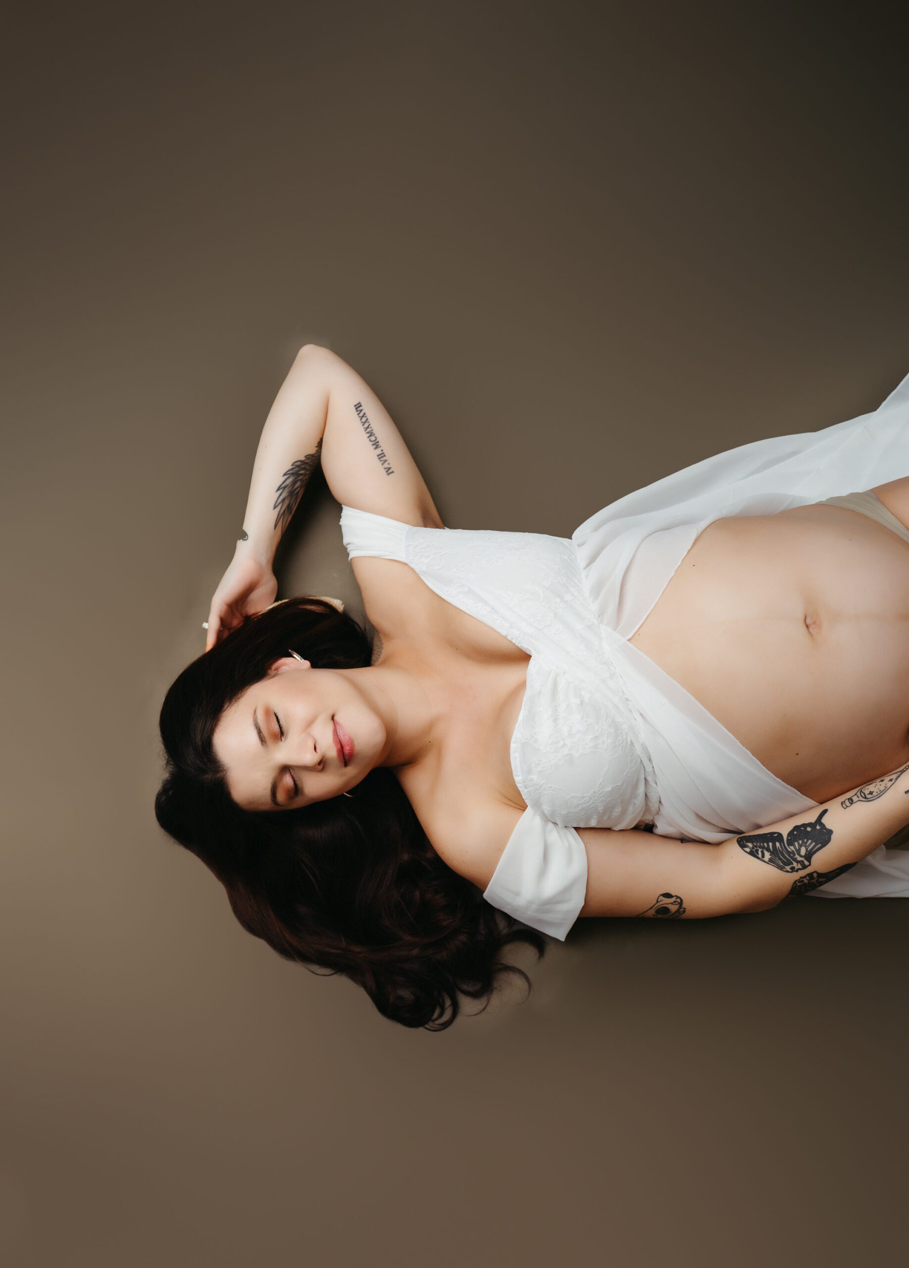 Beautiful pregnant woman laying down on the floor, embracing her baby bump with a soft smile.